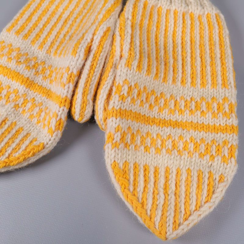 Närbild på stickat mönster på tumvantar i gult och vitt