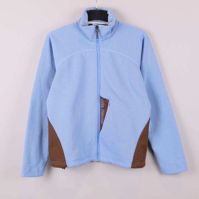 Ljusblå fleecejacka med bruna detaljer framtill hänger på galge