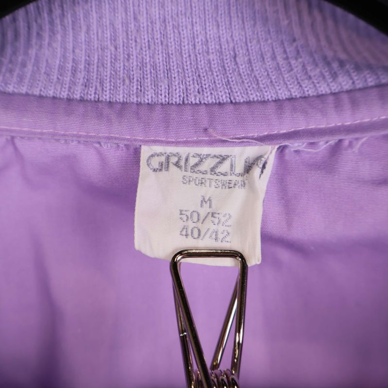 Närbild av etikett på lila jacka med storlek M