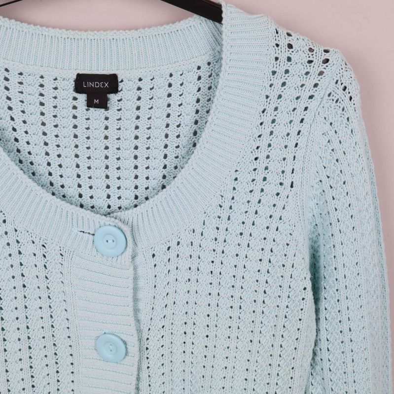 Närbild på stickat mönster och knappar i koftans överdel