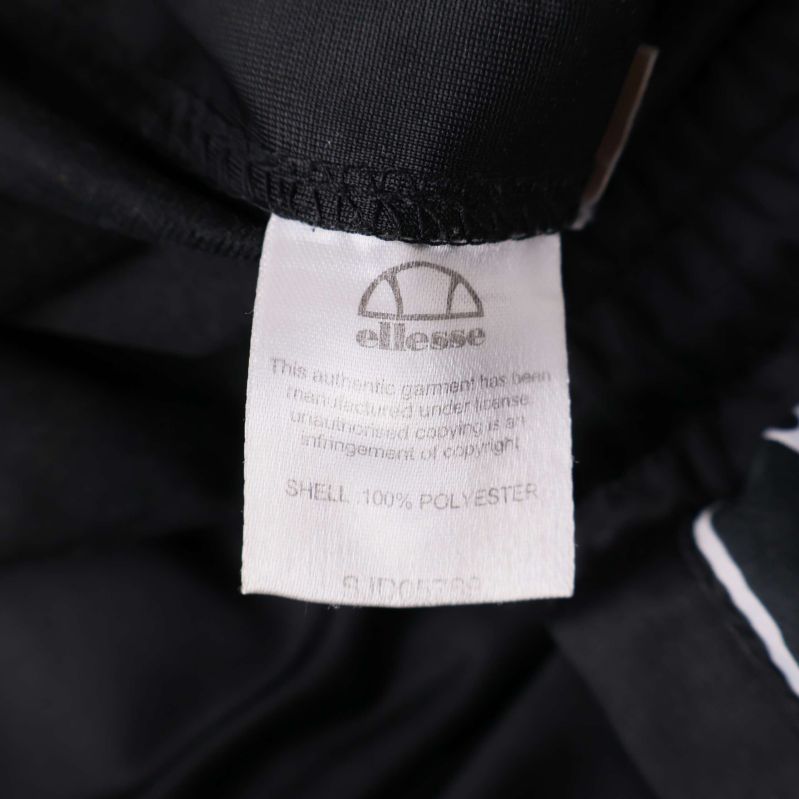 Materiallapp med text: shell 100% polyester och Ellesse-logotyp