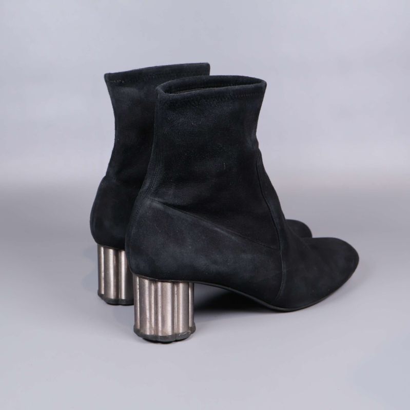 Bakre vy av svarta mockastövletter och cylinderformad klack i metallton