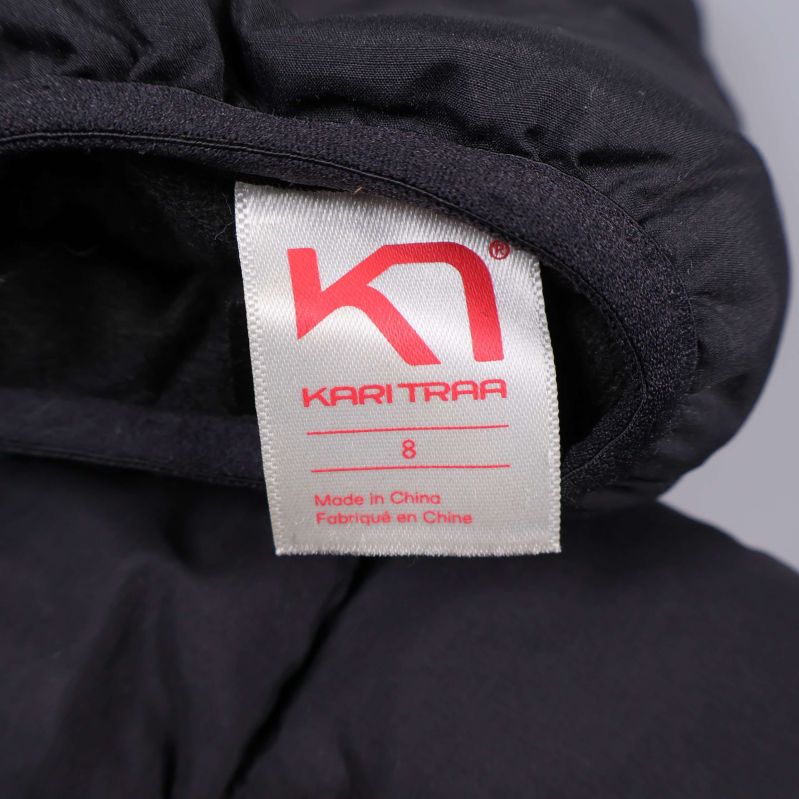 Vit etikett i tumvanten med röd text Kari Traa