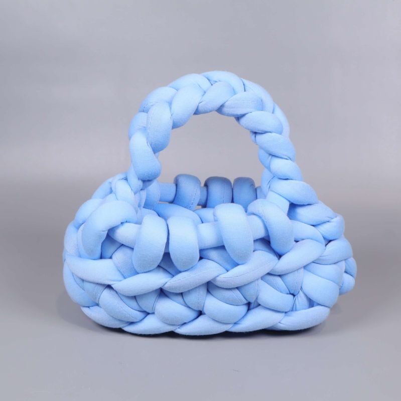 Framsidan av en ljusblå stickad handväska med tjocka flätor