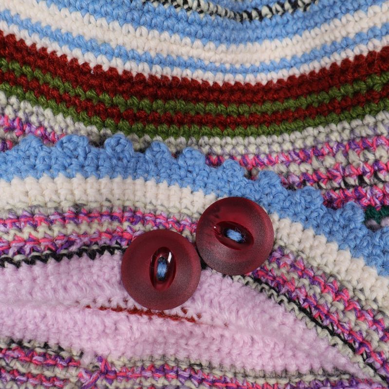 Närbild på blå och rosa virkad kant och röda knappar