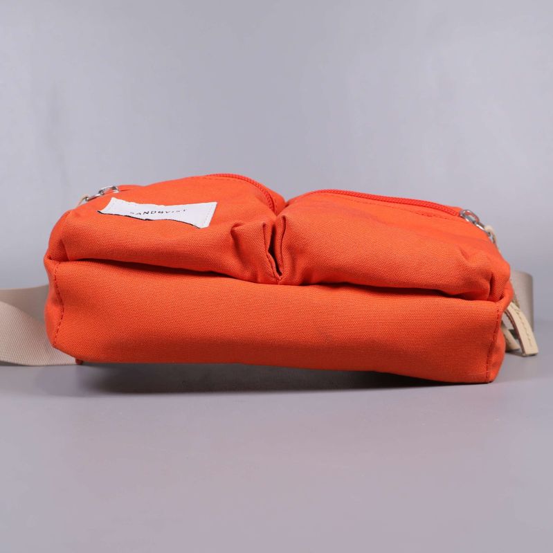 Orange axelväska liggandes med synliga fickor