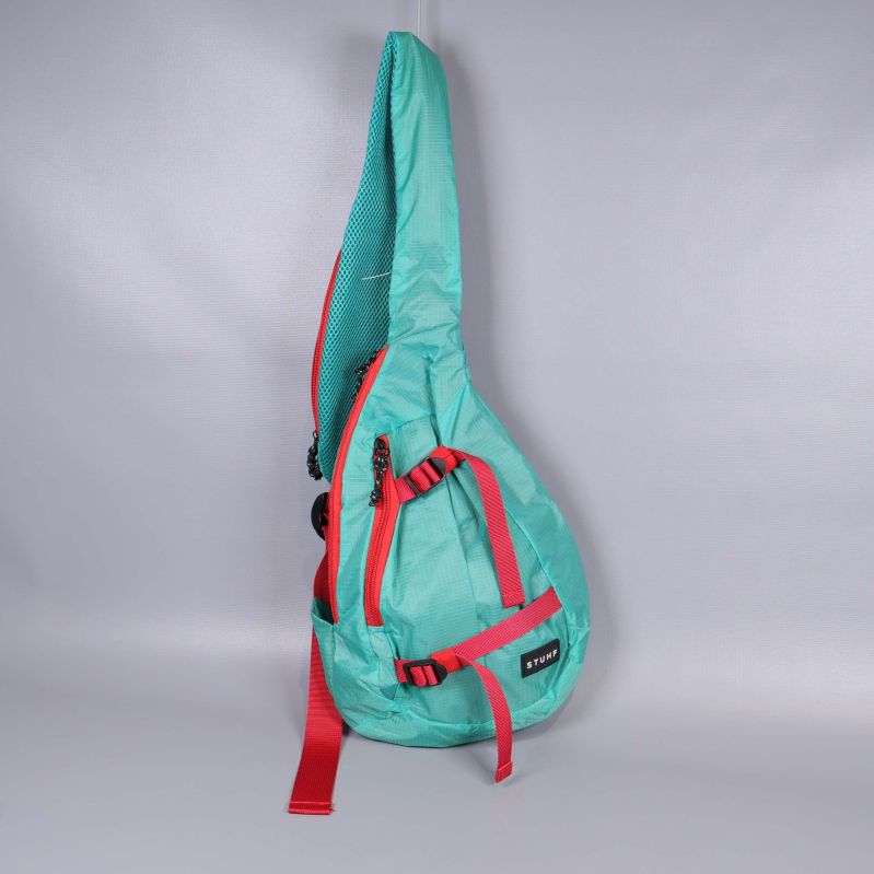 Turkos axelremsväska med röda remmar stående mot ljus bakgrund