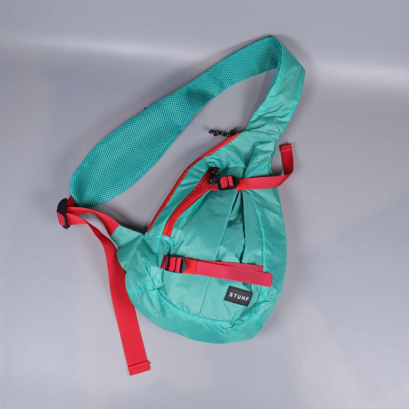Turkos axelremsväska med röd blixtlås och rem i diagonal vy