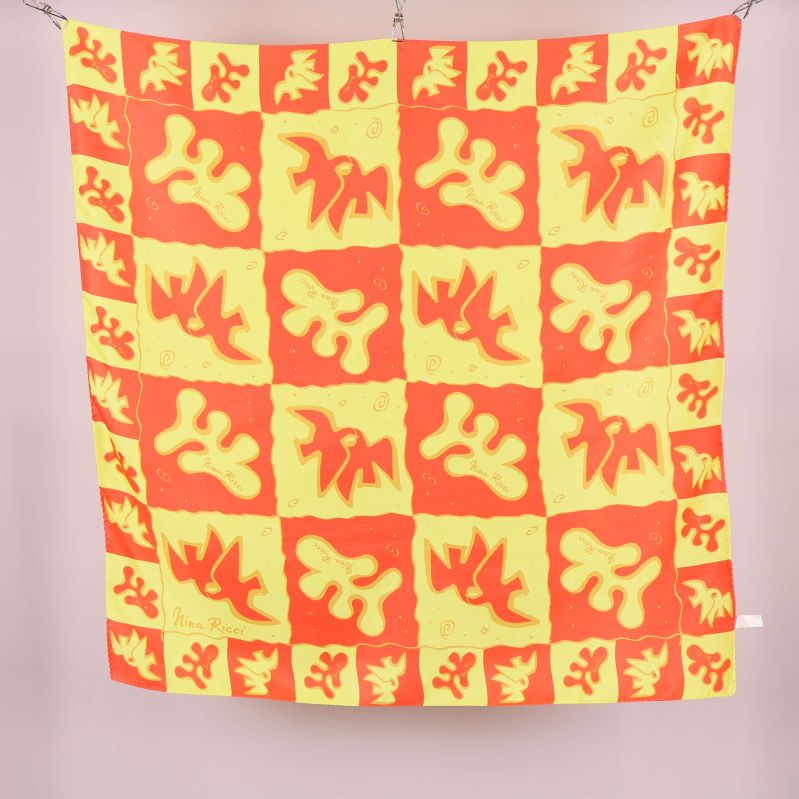 Stor scarf med rött och gult grafiskt mönster upphängd mot ljus bakgrund