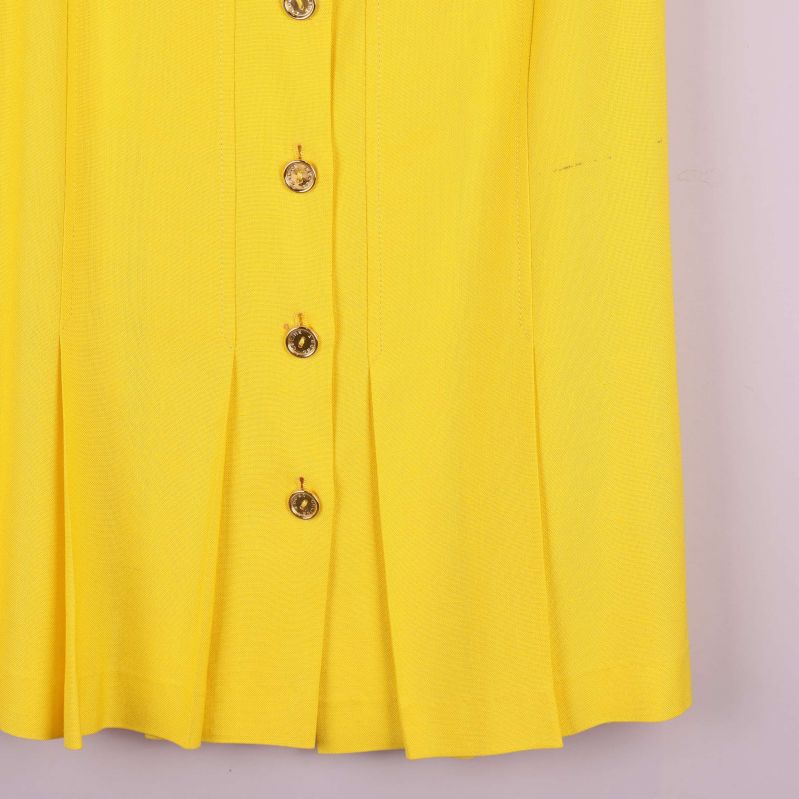 Detaljbild på nederkant och veck fram på gul kjol