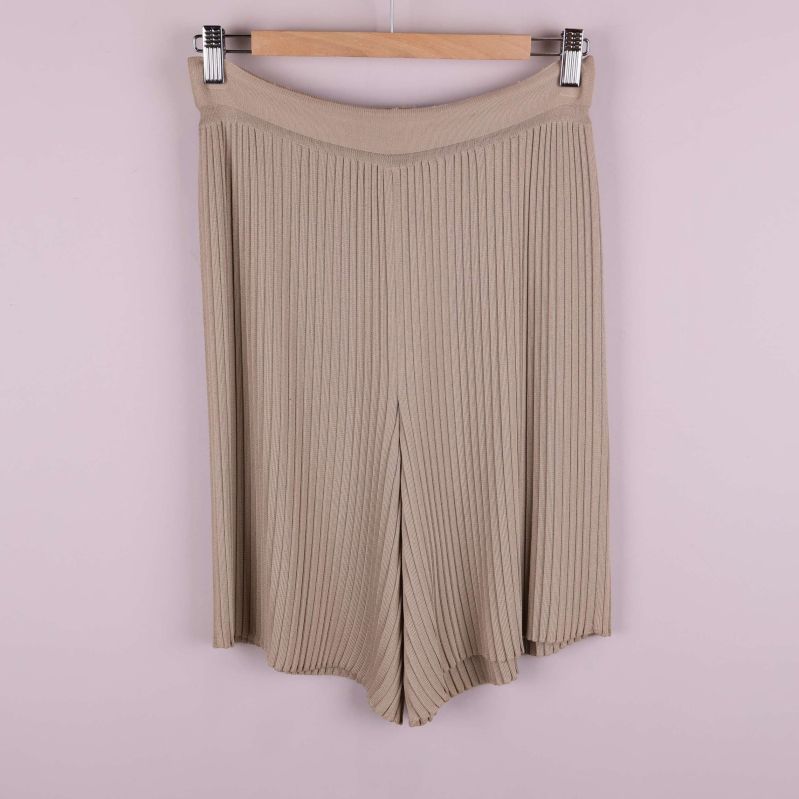 Beige plisserade shorts hänger på galge mot ljus bakgrund