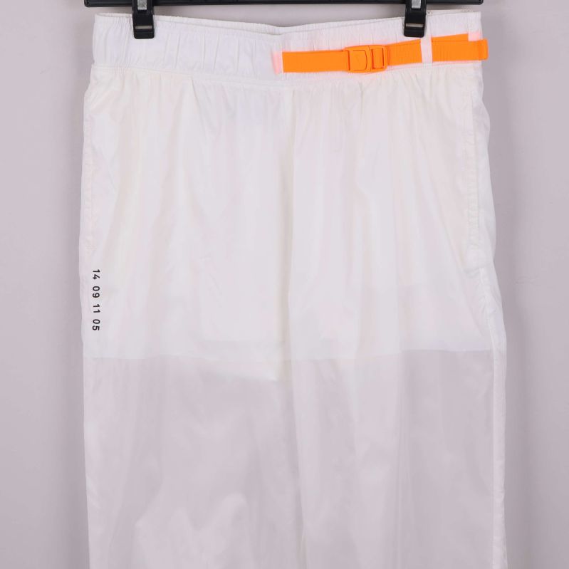 Närbild på orange rem och tryck på vita byxor