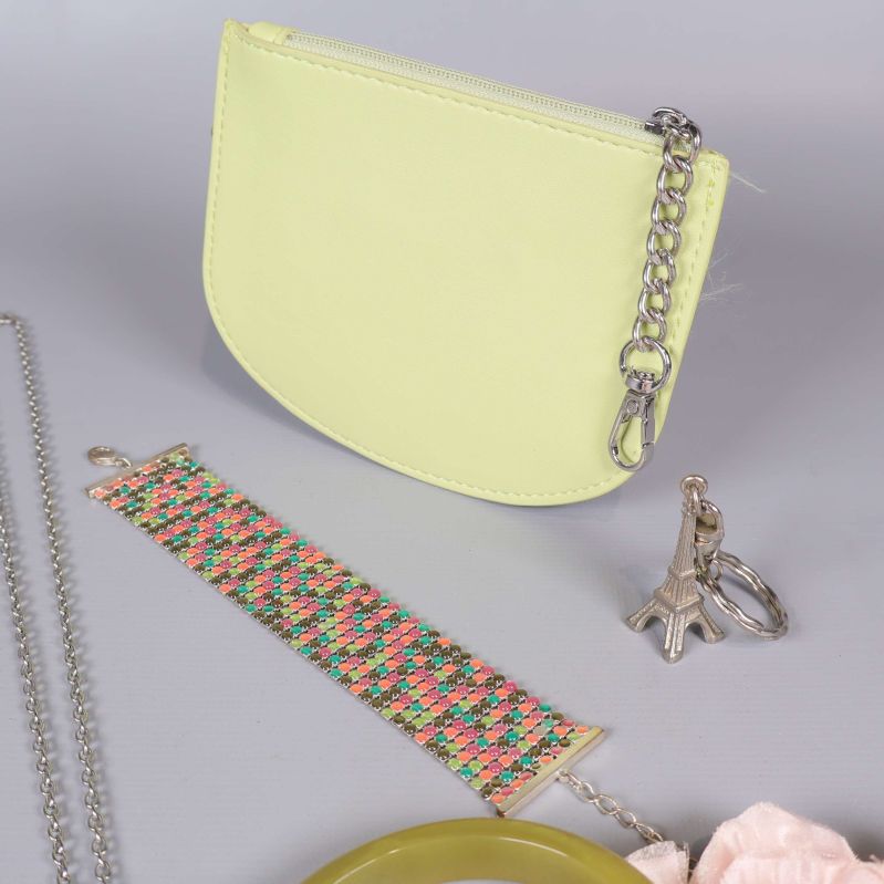 Närbild på litet ljusgult fodral, mönstrat armband, och ringar