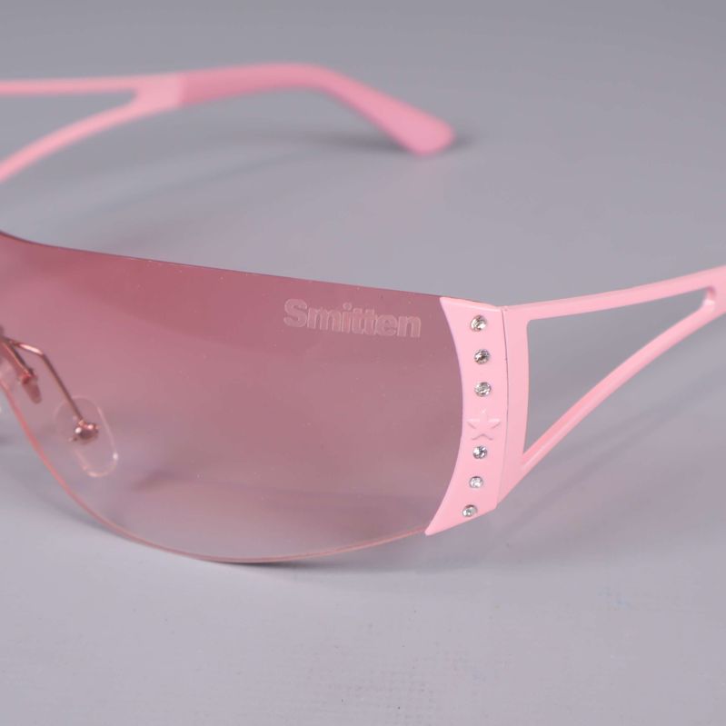 Närbild solglasögon med logotyp och strassdetaljer på rosa båge