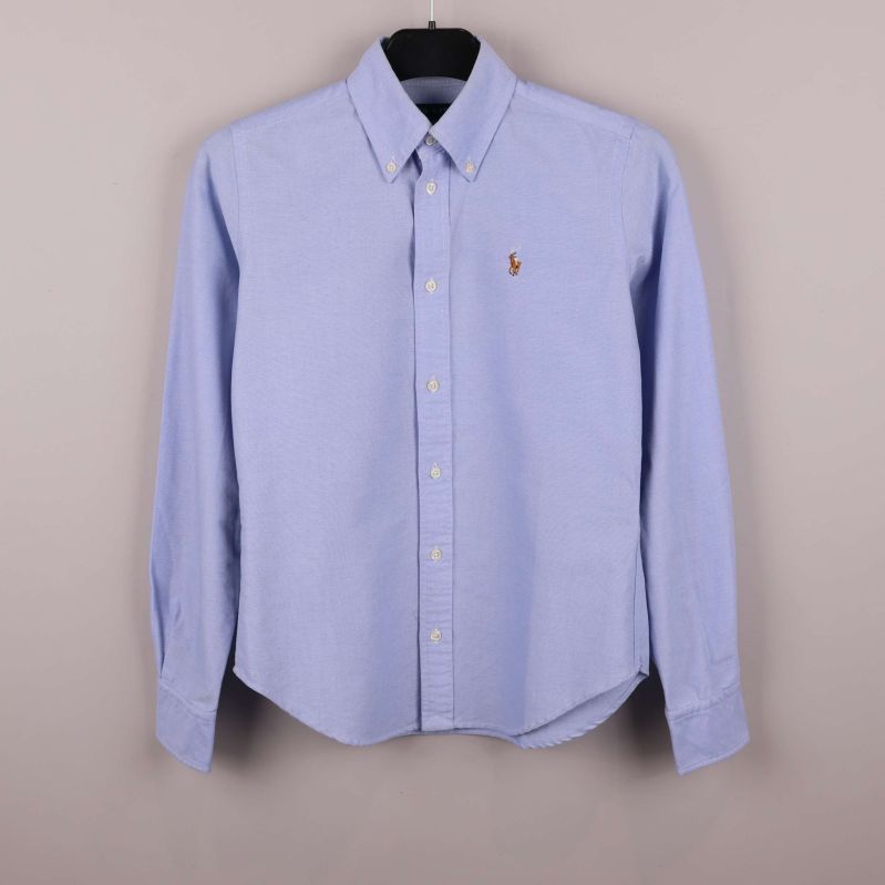 Ljusblå skjorta på galge med knappslå och broderad logga