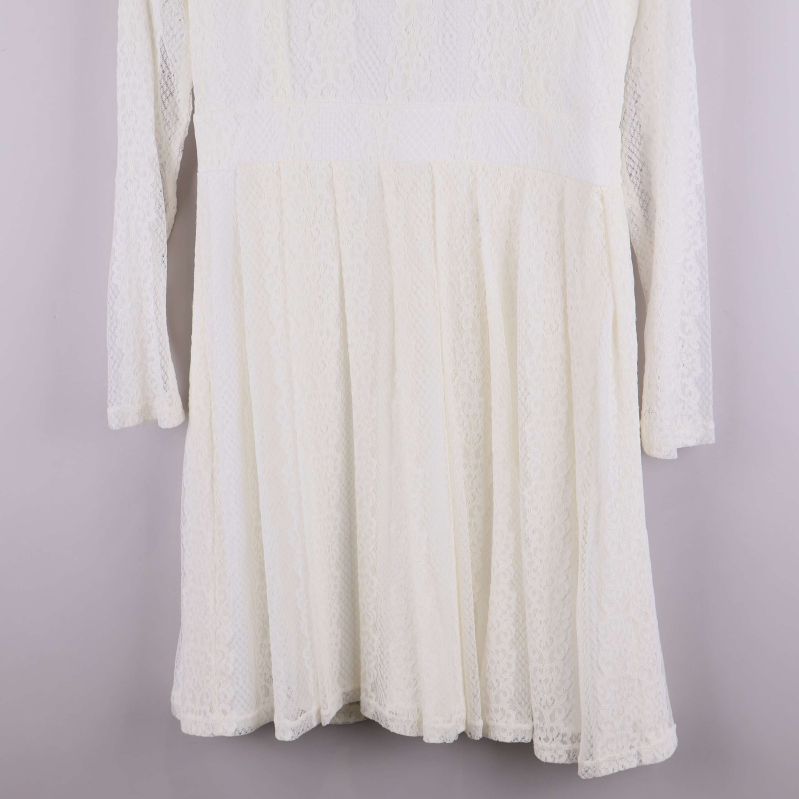 Närbild på kjoldel av vit spetsklänning med plisserat fall