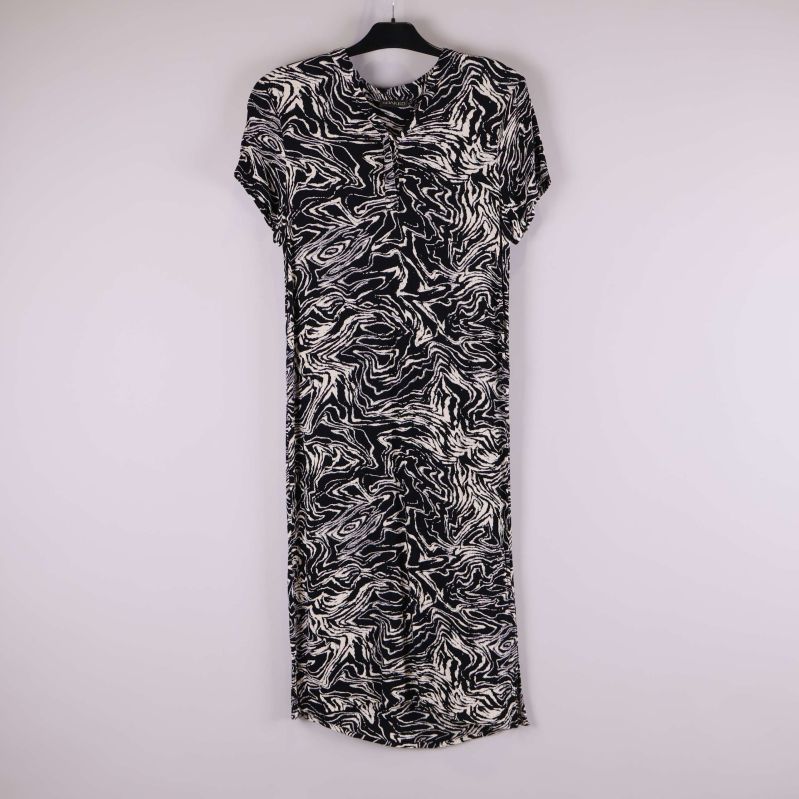 Svartvit mönstrad klänning hänger på galge mot ljus bakgrund