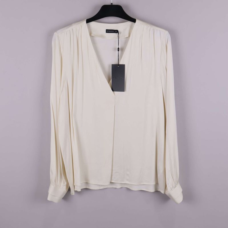 Ljus långärmad blus på galge mot grå bakgrund