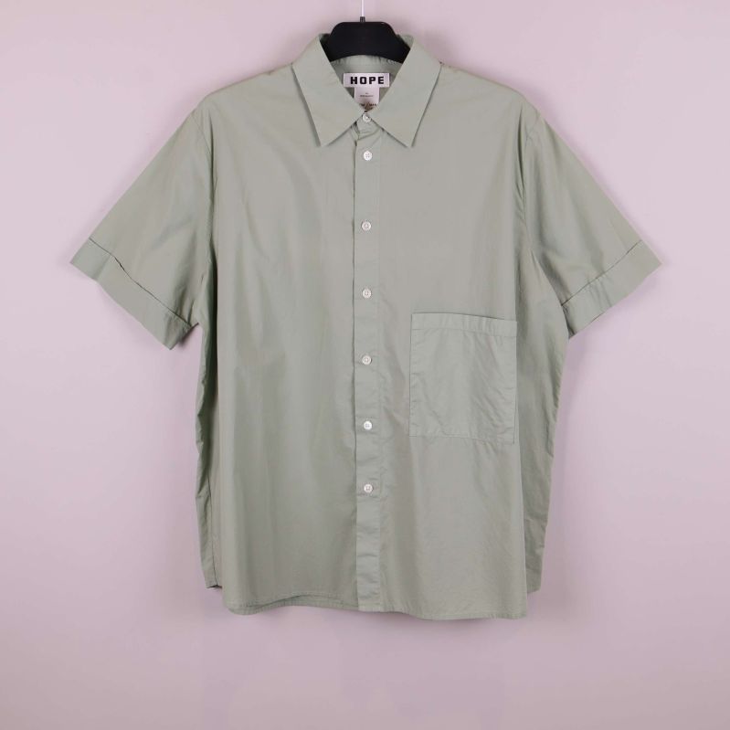 Ljusgrön kortärmad skjorta hänger mot rosa bakgrund