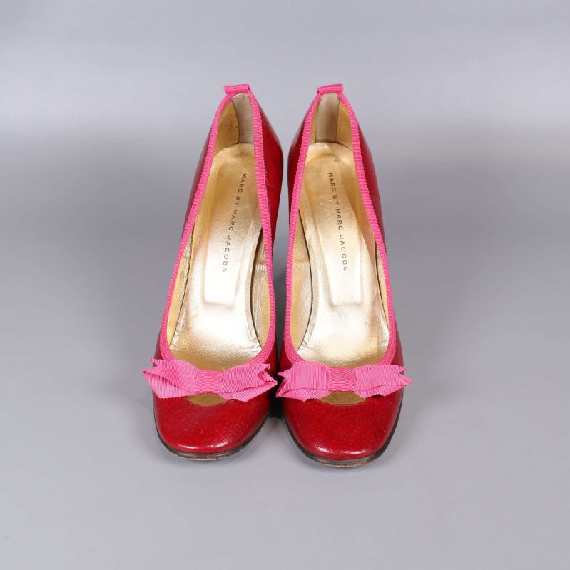 Pumps framifrån med rosa rosett och röd bas