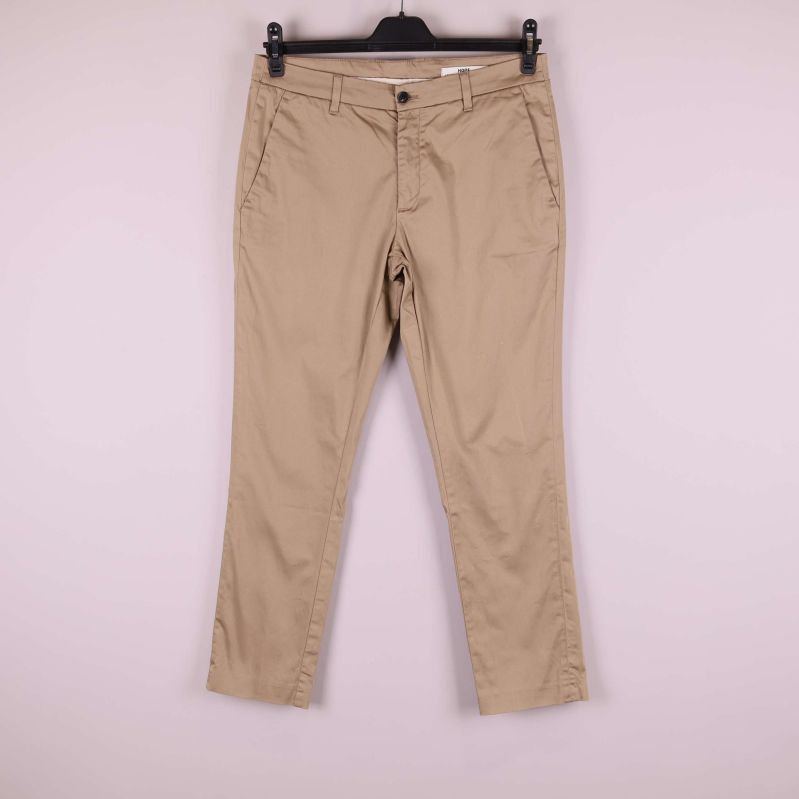 Beiga byxor upphängda mot ljus bakgrund, framifrån