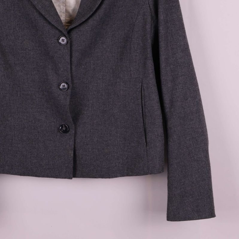 Kavajens nederkant och ärm, grå tygstruktur synlig