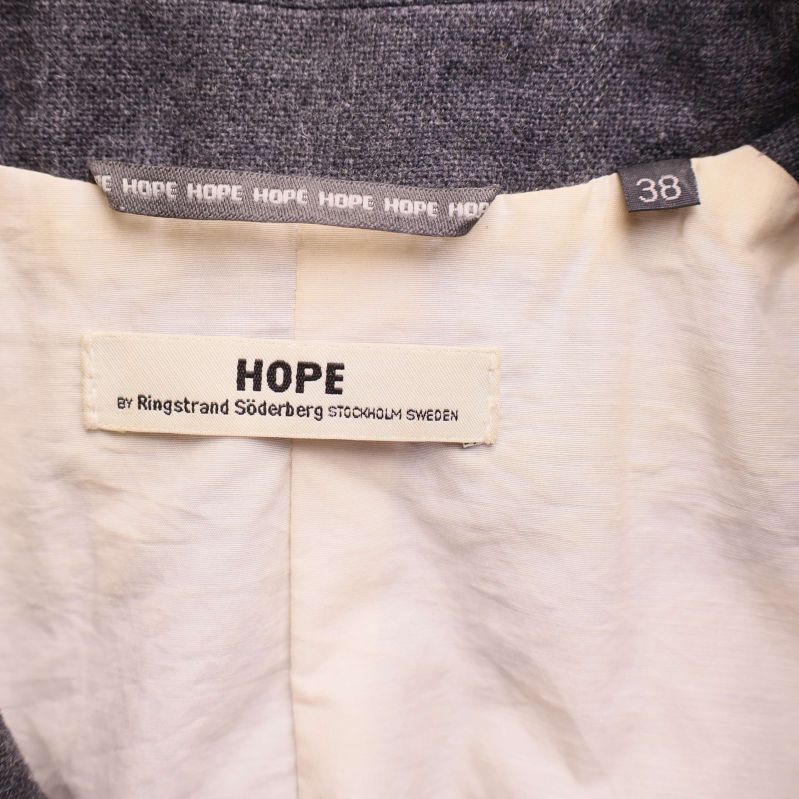Storleksetikett 38 och HOPE-märke i kavajens nacke