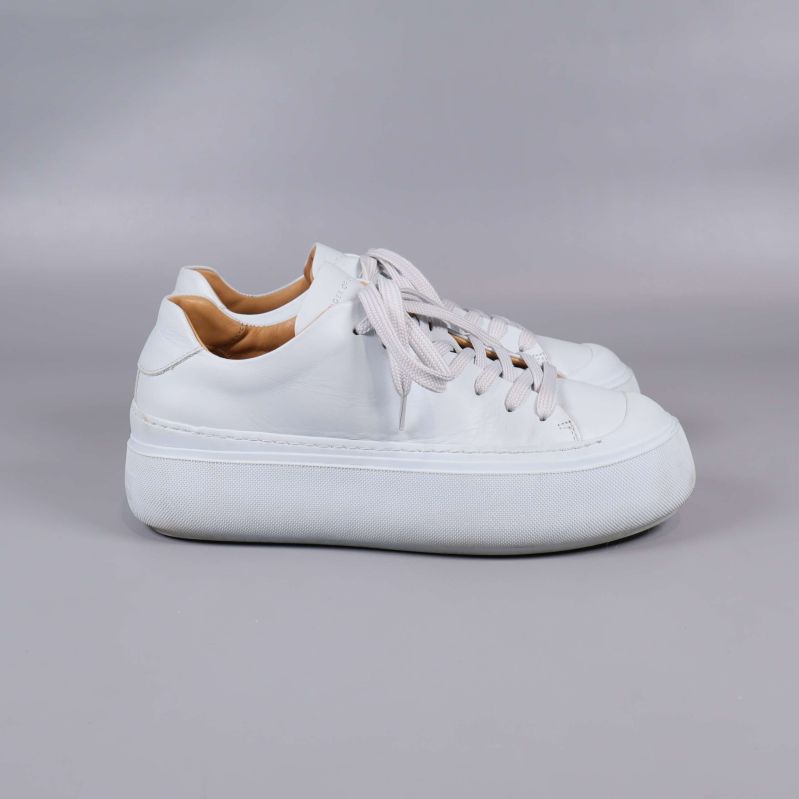 Vita sneakers i profil på grå bakgrund