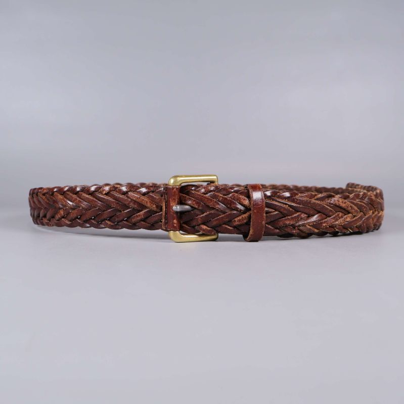 Helt flätat brunt läderbälte med mässingsspänne mot grå bakgrund