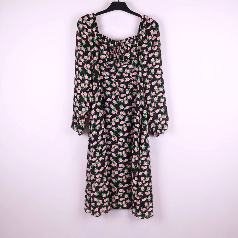 Blommig klänning med långa ärmar upphängd på galge mot ljus bakgrund