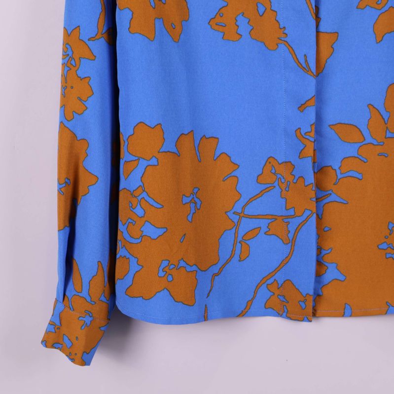 Närbild på skjortans nederkant och ärm i blått med bruna blommor