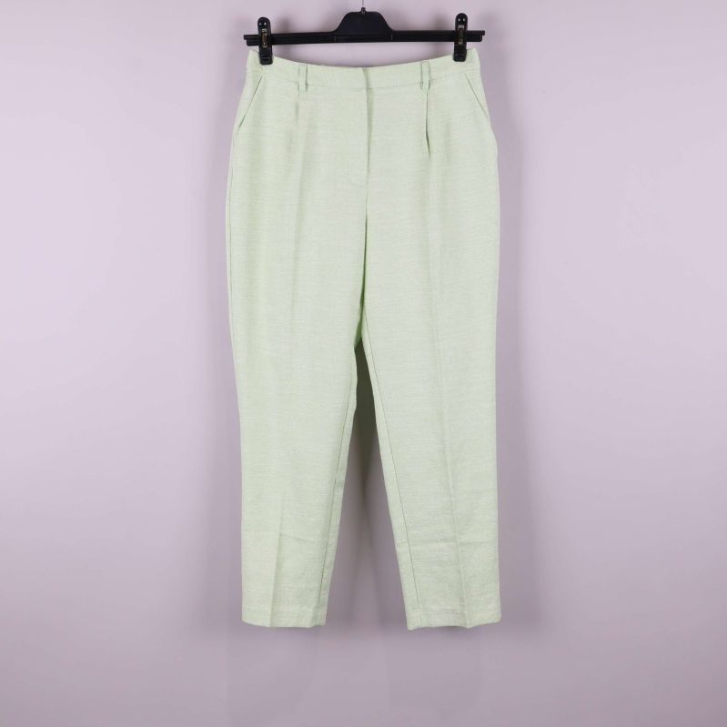 Ljusgröna byxor upphängda mot ljus bakgrund, helbild framifrån