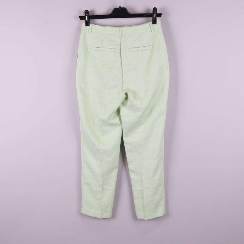 Ljusgröna byxor upphängda mot ljus bakgrund, helbild bakifrån