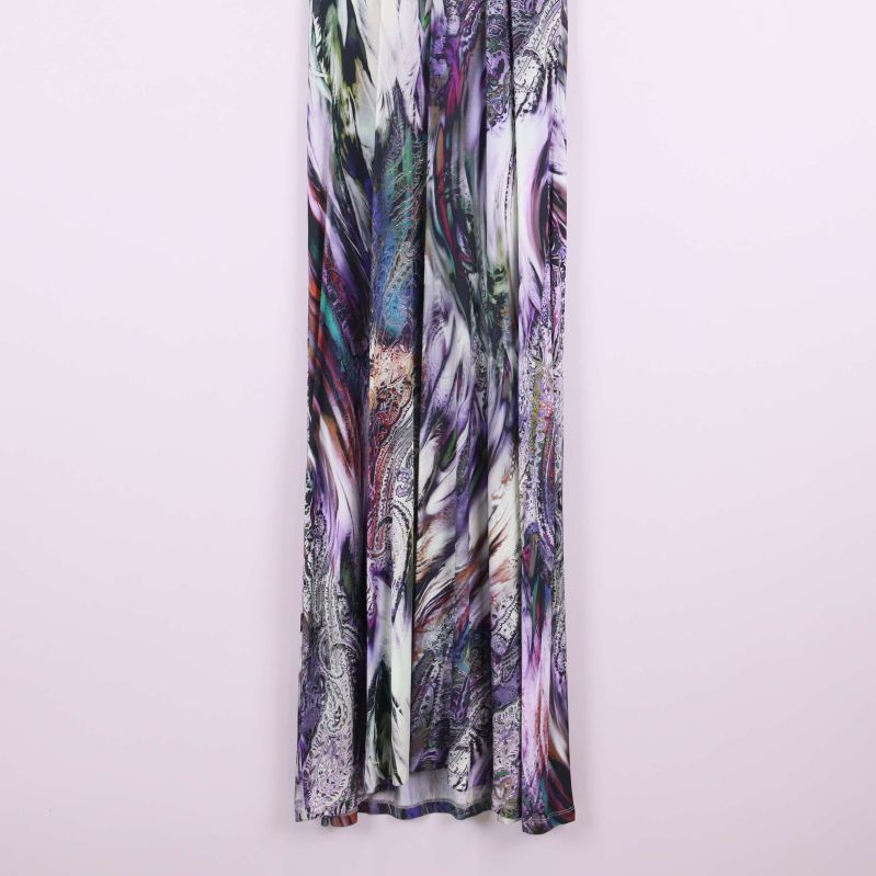 Nederdel av långklänning i flerfärgat tyg mot ljus vägg