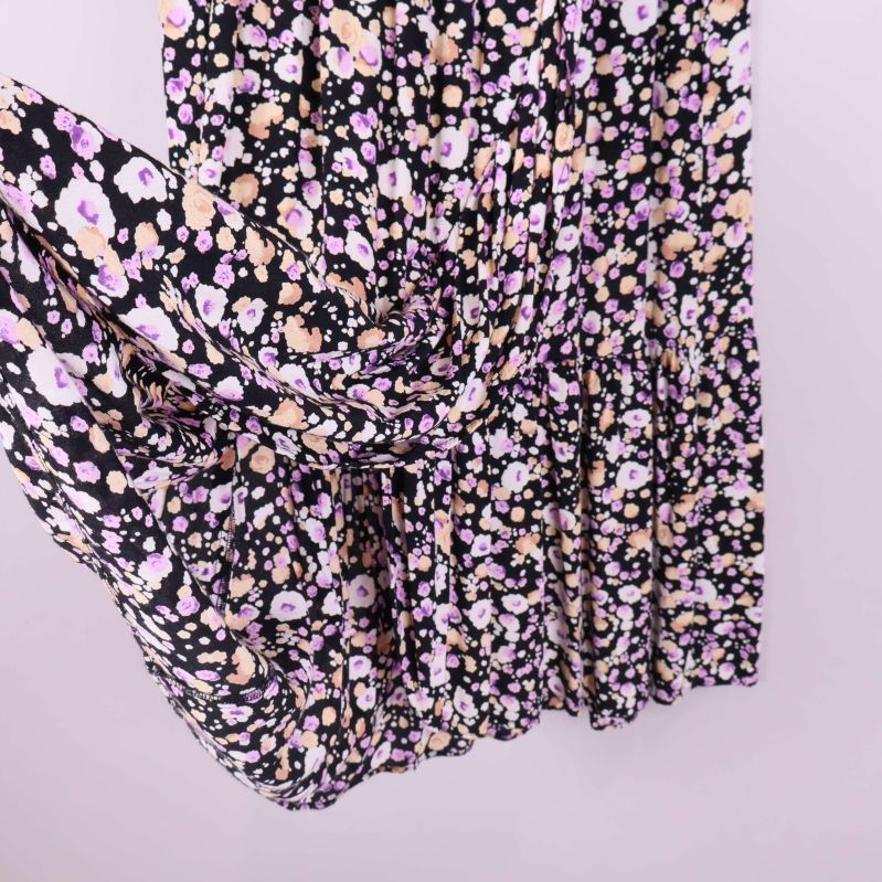 Plisserad kjol i svart med beige och lila blommor sedd från sidan