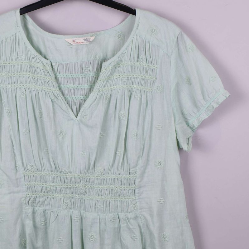 Närbild på v-ringning och smockdetaljer på ljusgrön blus