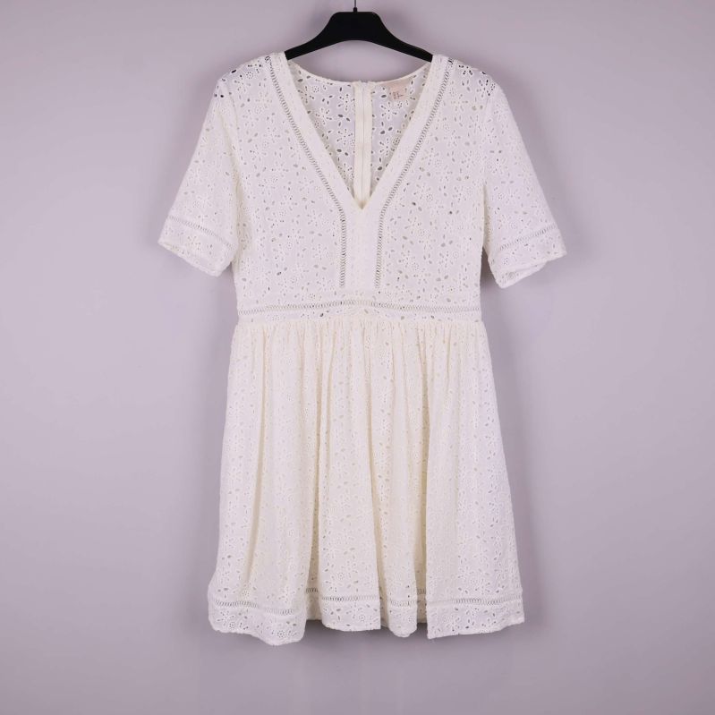 Kort vit klänning med V-ringning och broderade detaljer hängande på galge