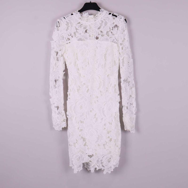 Vit spetsklänning med lång ärm framifrån mot ljus bakgrund