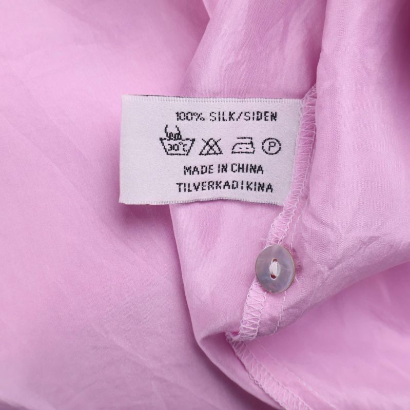 Materialetikett med texten 100% Siden på rosa skjorta
