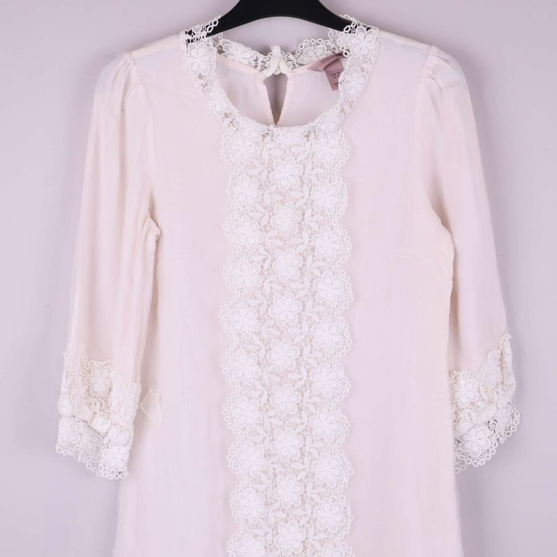 Närbild på klänningens spetsdetaljer framtill vid hals och ärmslut