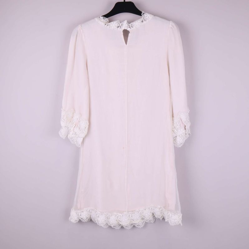 Vit klänning med spets i helfigur bakifrån på galge