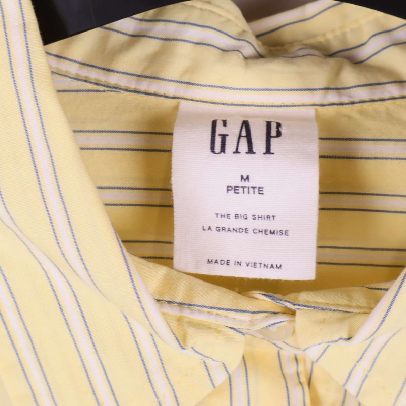 Närbild på GAP-märkesetikett och krage i ljusgul skjorta