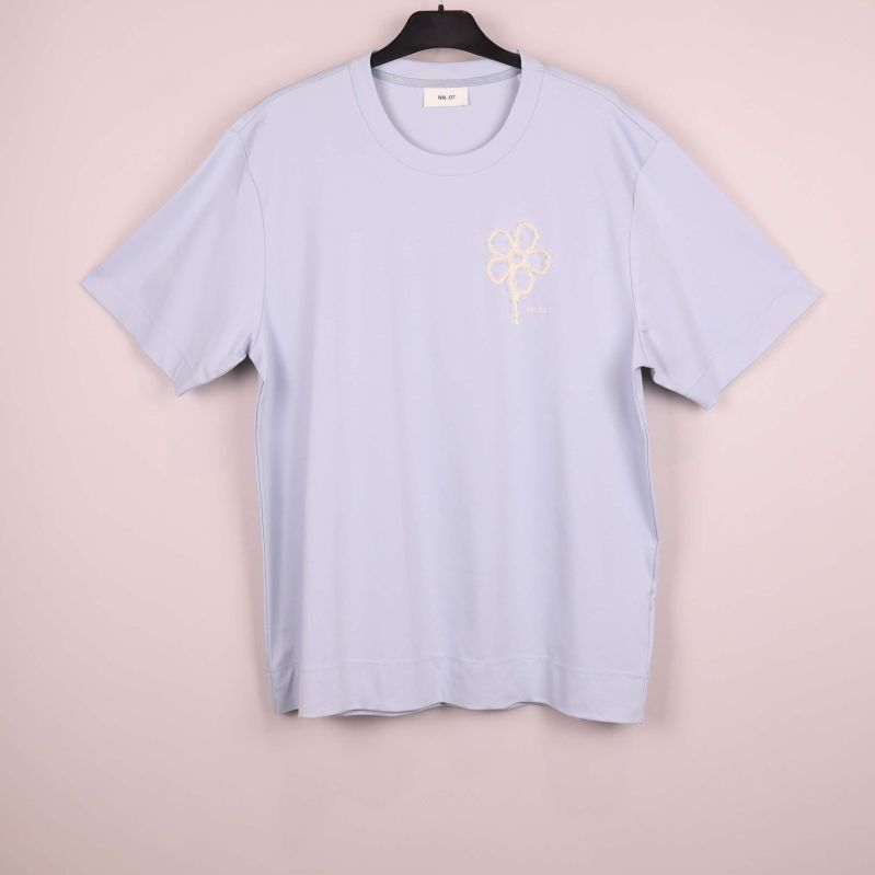 Ljusst blå t-shirt på galge mot rosa bakgrund