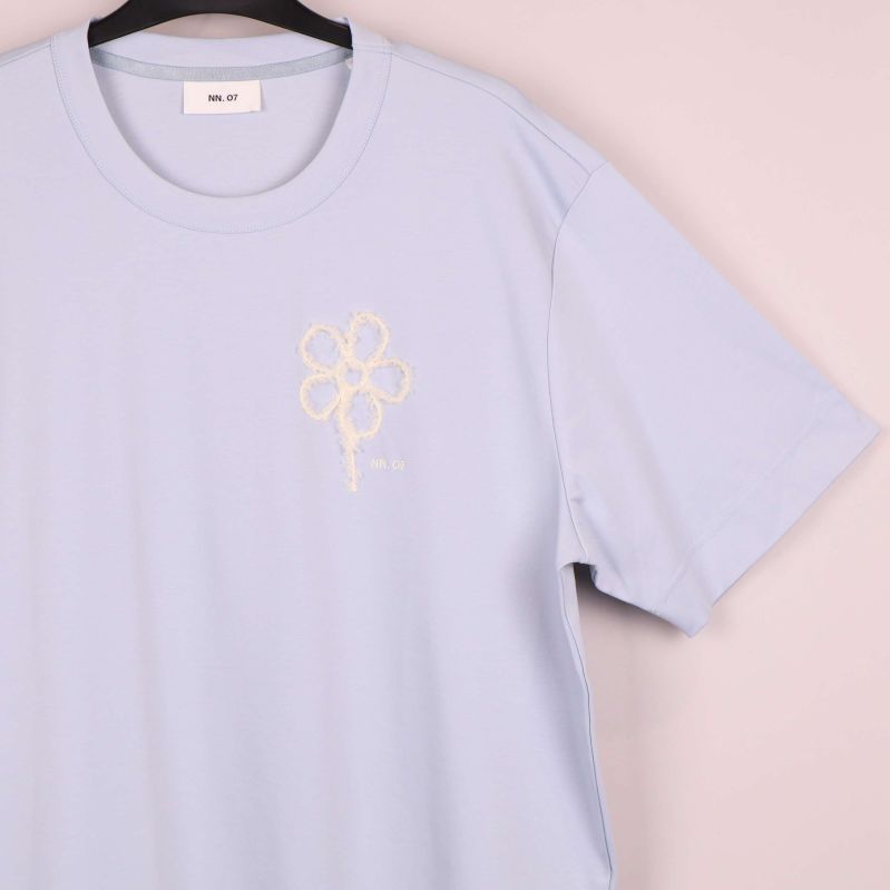 Närbild på broderad vit blomma på t-shirtens vänstra bröst