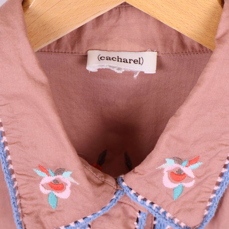 Närbild på krage med blommigt broderi och Cacharel-märke