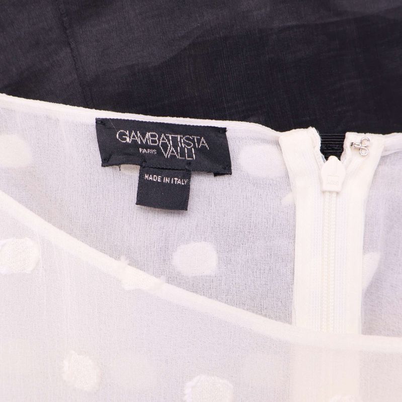 Närbild på Giambattista Valli label och vit dragkedja på toppen