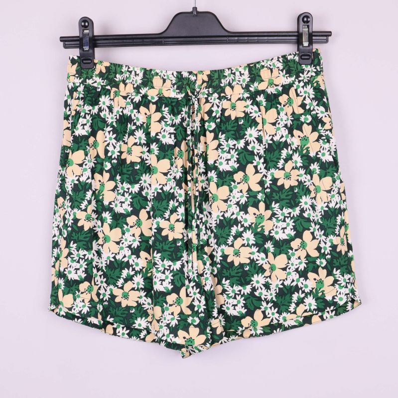 Shorts med grönt, vitt och beige blommönster hänger på galge