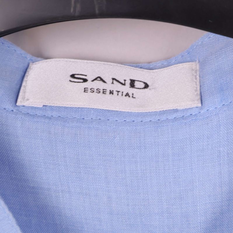 Närbild på vit Sand Essential-etikett i ljusblå tunika