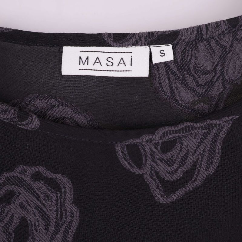 Närbild på Masai-logga samt storlek S i nacken på blusen