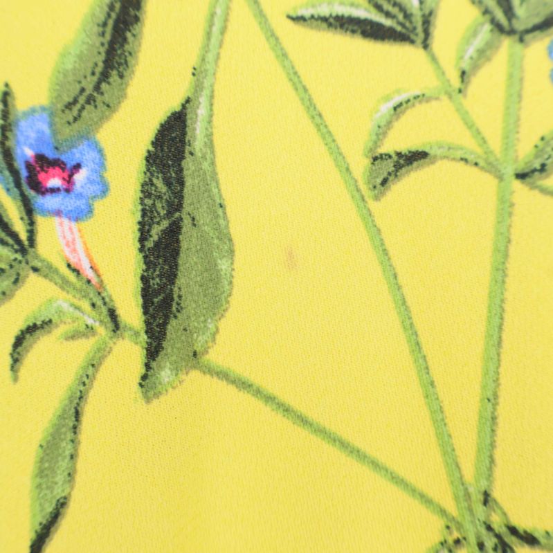 Detalj av gul klänning med blommönster och en liten fläck